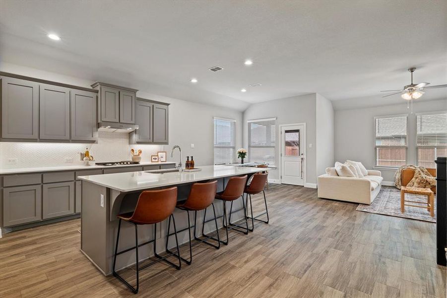 Kitchen with light wood-type flooring, ceiling fan, a kitchen bar, sink, and a center island with sink