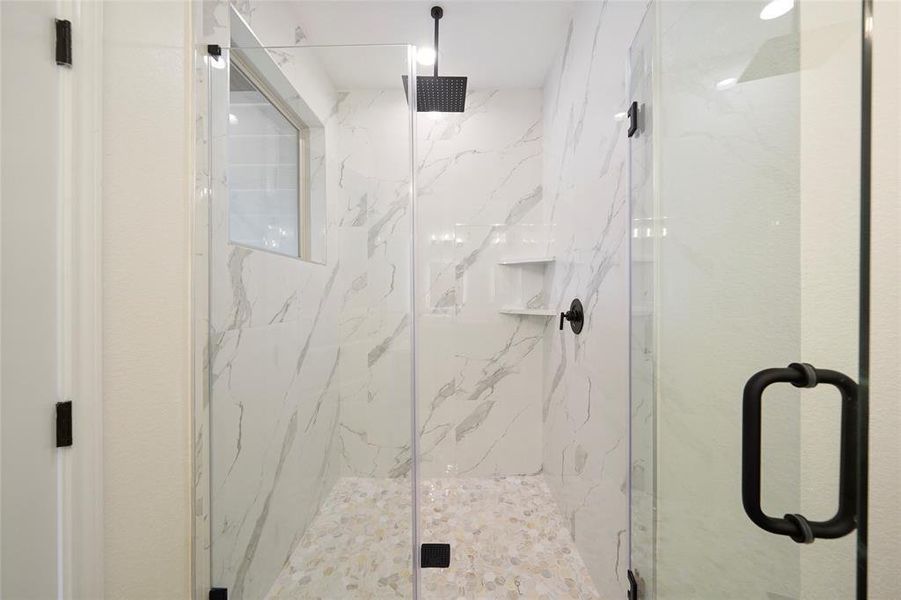 Shower in the primary bath with shelving for products, rain head shower and seamless glass shower enclosure.