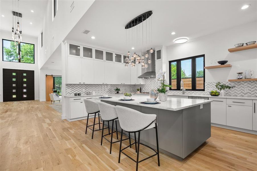 Kitchen with pendant lighting, a center island, white cabinetry, wall chimney range hood, and a kitchen breakfast bar