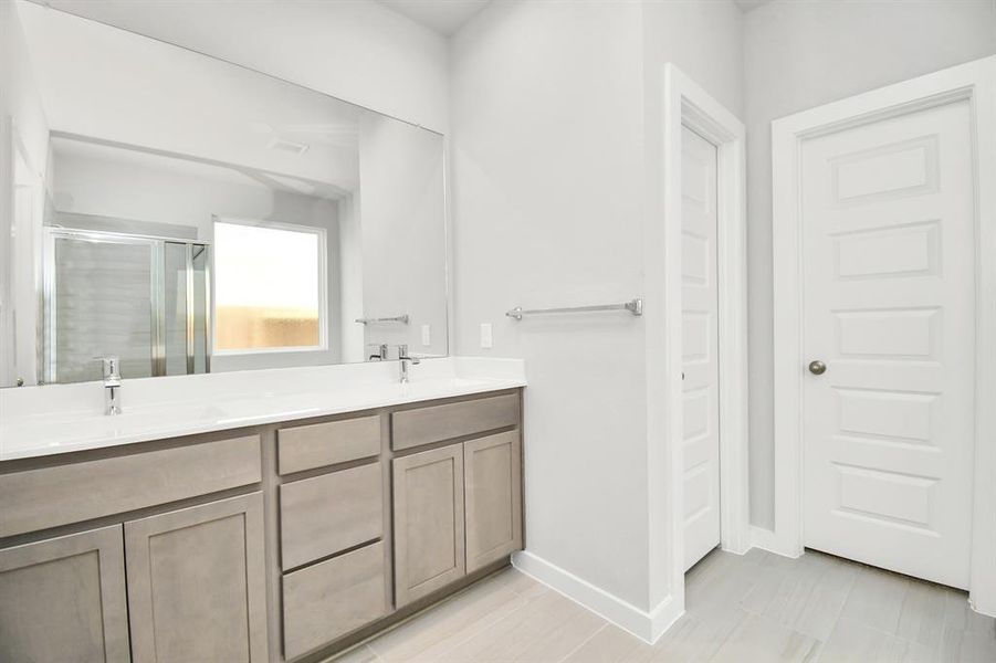 The sophisticated vanity, featuring double sinks, dark-colored countertops, contemporary hardware, and bright recessed lighting, adds both style and functionality to the space. Sample photo of completed home with similar floor plan. Actual colors and selections may vary.