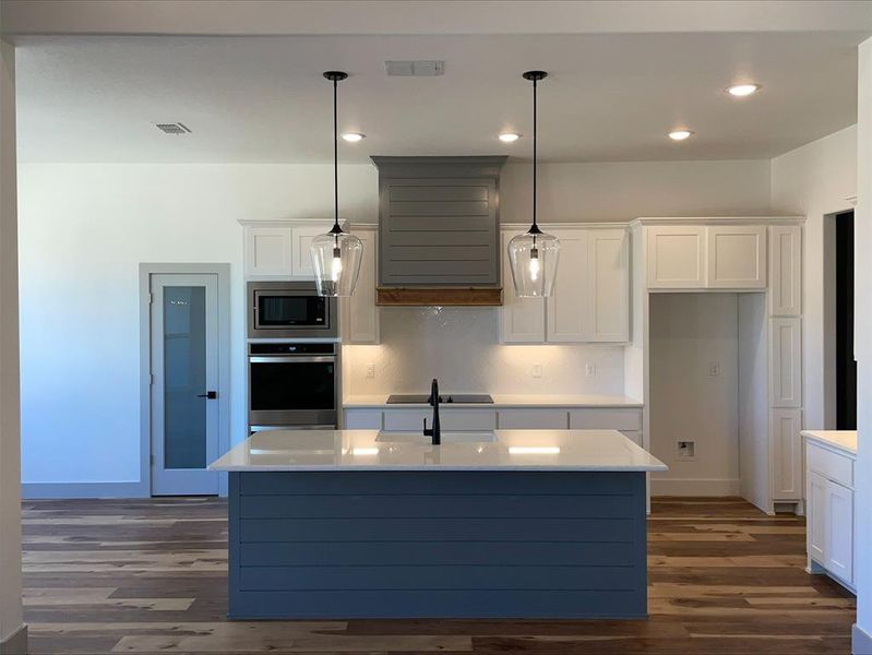 Kitchen featuring stainless steel appliances, a center island with sink, pendant lighting, dark hardwood / wood-style flooring, and white cabinetry