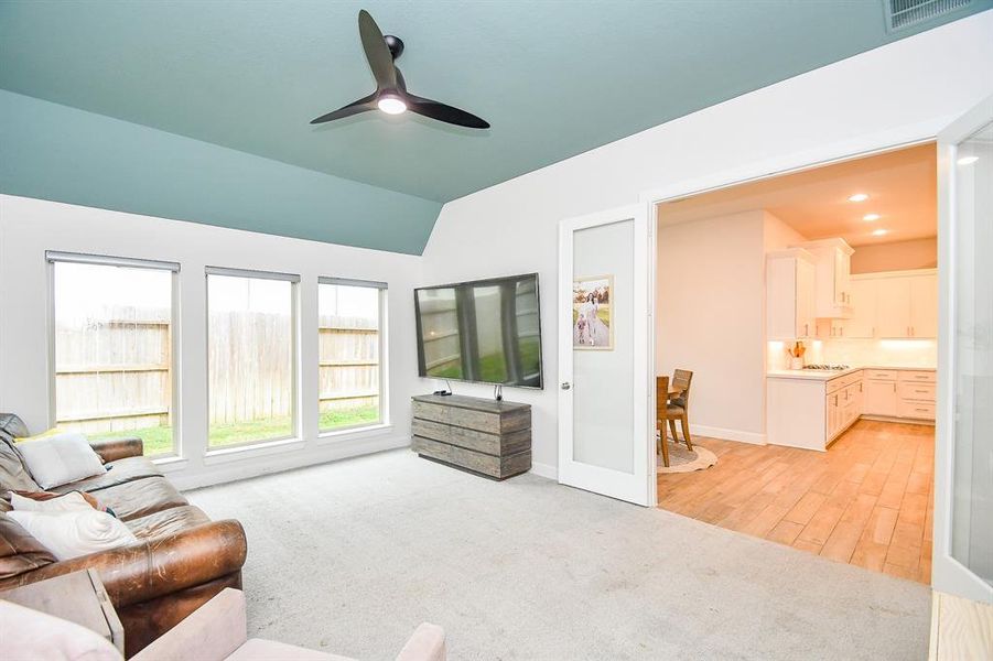 Spacious, well-lit game room featuring a vaulted ceiling with a contrasting paint accent, large windows providing ample natural light, double doors with glass accent. New carpet creates a clean, inviting space. a ceiling fan.