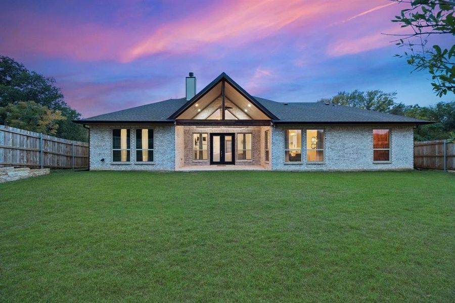 Back house at dusk with french doors and a lawn