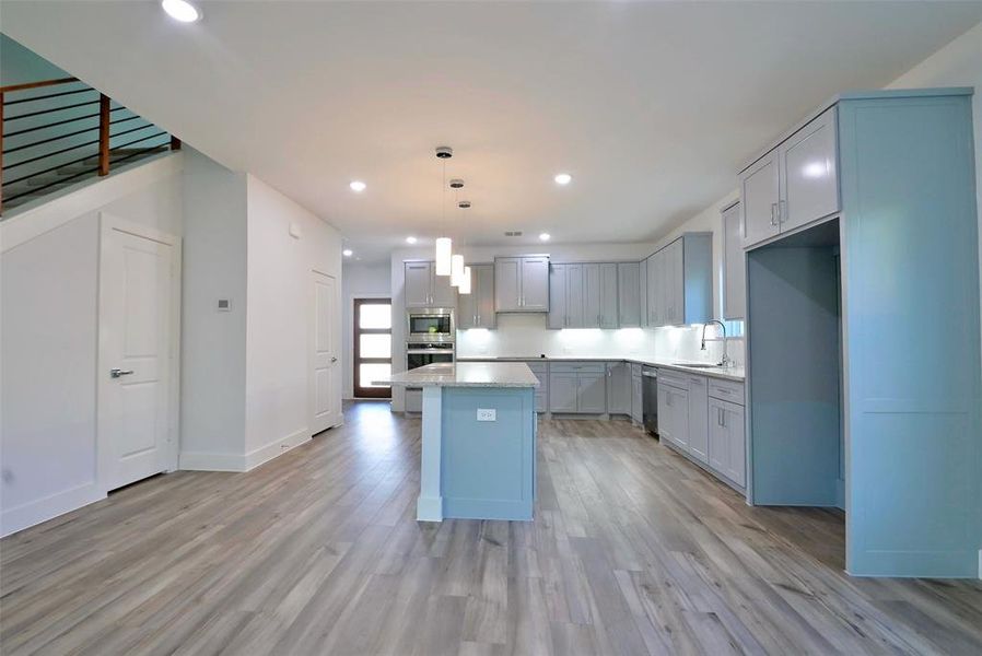 Kitchen with hanging light fixtures, light hardwood / wood-style floors, a kitchen island, and sink