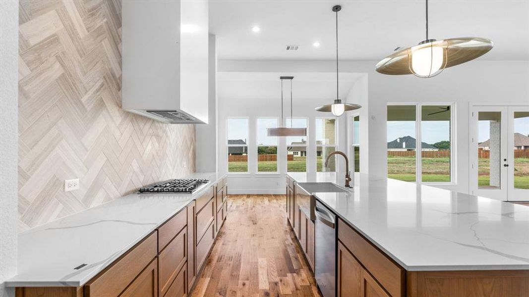 Kitchen featuring appliances with stainless steel finishes, hanging light fixtures, light hardwood / wood-style floors, light stone counters, and sink