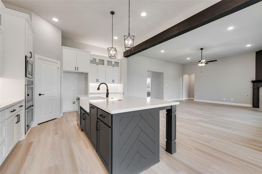 Kitchen with pendant lighting, beamed ceiling, white cabinets, a center island with sink, and ceiling fan