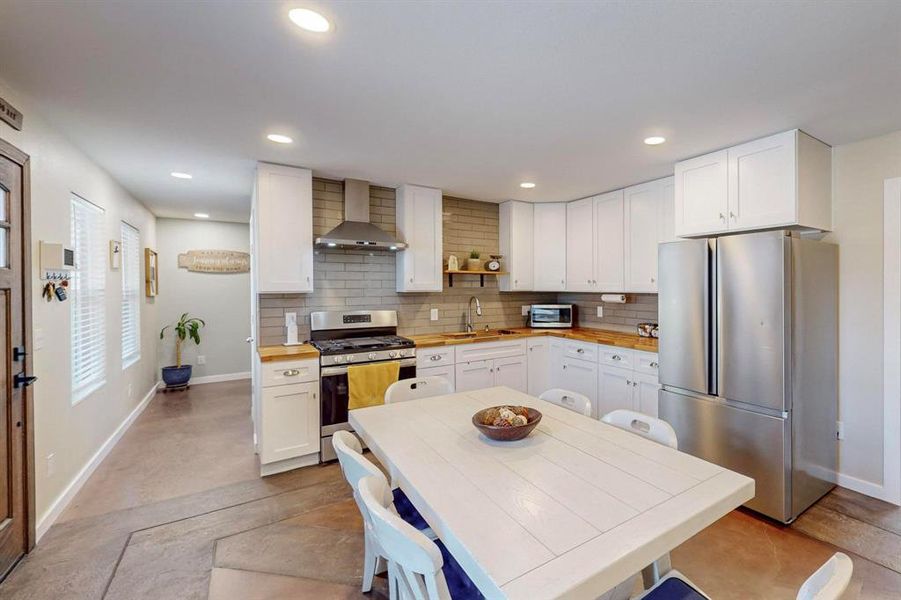 Kitchen featuring tasteful backsplash, white cabinetry, sink, wall chimney exhaust hood, and stainless steel appliances