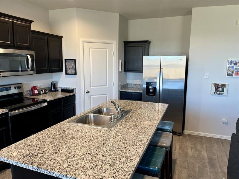 Kitchen with sink, hardwood / wood-style floors, an island with sink, a kitchen bar, and appliances with stainless steel finishes