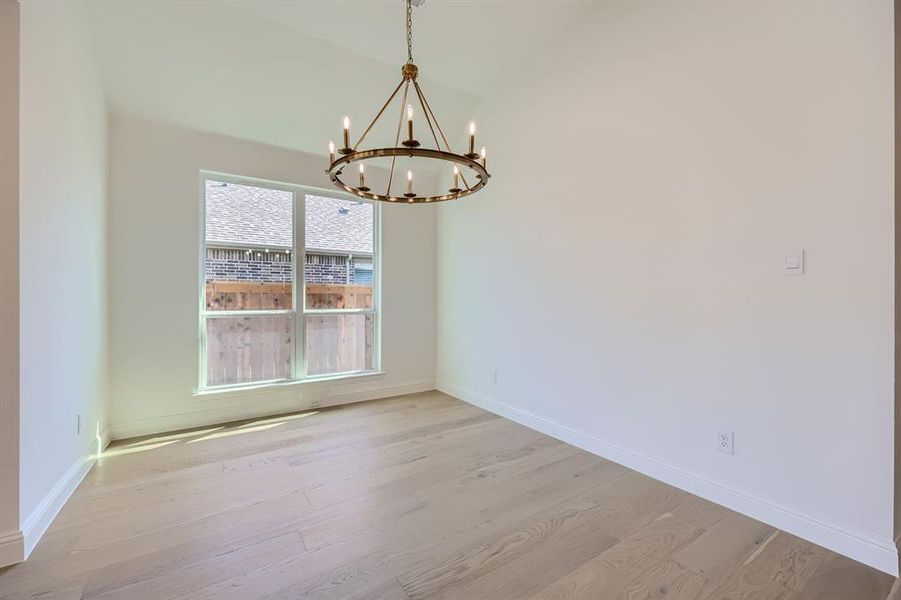 Spare room featuring light wood-type flooring, vaulted ceiling, and a chandelier