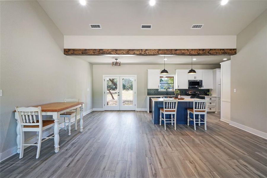 Kitchen with hardwood / wood-style flooring, appliances with stainless steel finishes, white cabinetry, a breakfast bar area, and pendant lighting