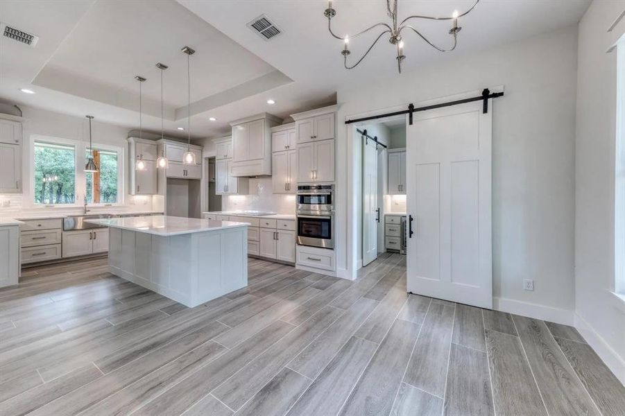 Kitchen featuring light hardwood / wood-style flooring, hanging light fixtures, a barn door, and a raised ceiling