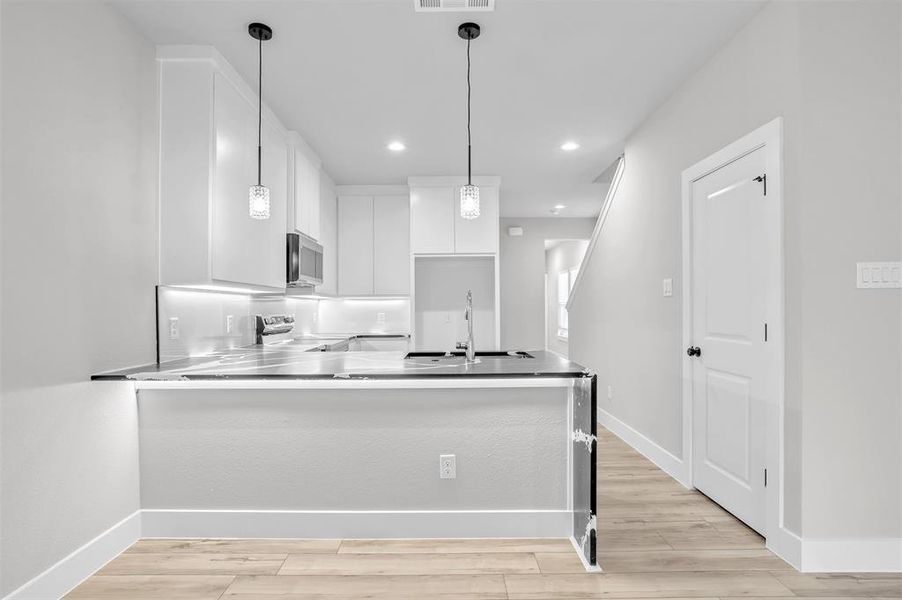 Kitchen with appliances with stainless steel finishes, white cabinetry, decorative light fixtures, and sink