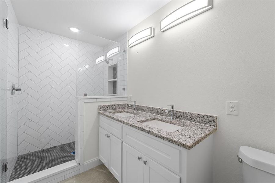 Bathroom with toilet, vanity, and tiled shower