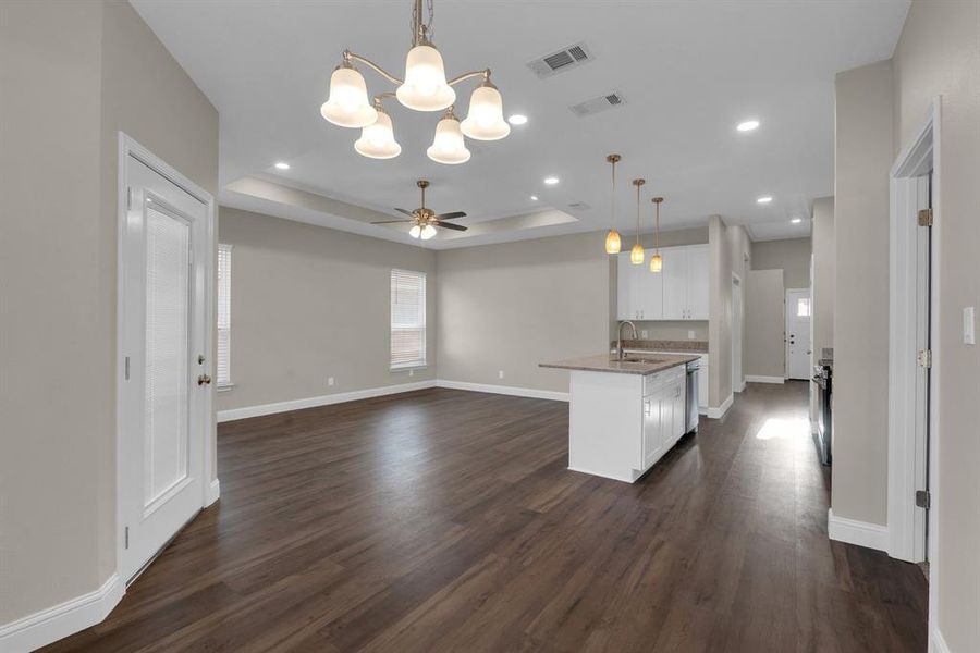 Kitchen with white cabinets, an island with sink, a raised ceiling, decorative light fixtures, and dark wood-type flooring