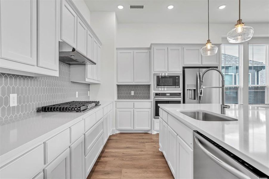 Kitchen featuring light wood-type flooring, backsplash, hanging light fixtures, appliances with stainless steel finishes, and sink