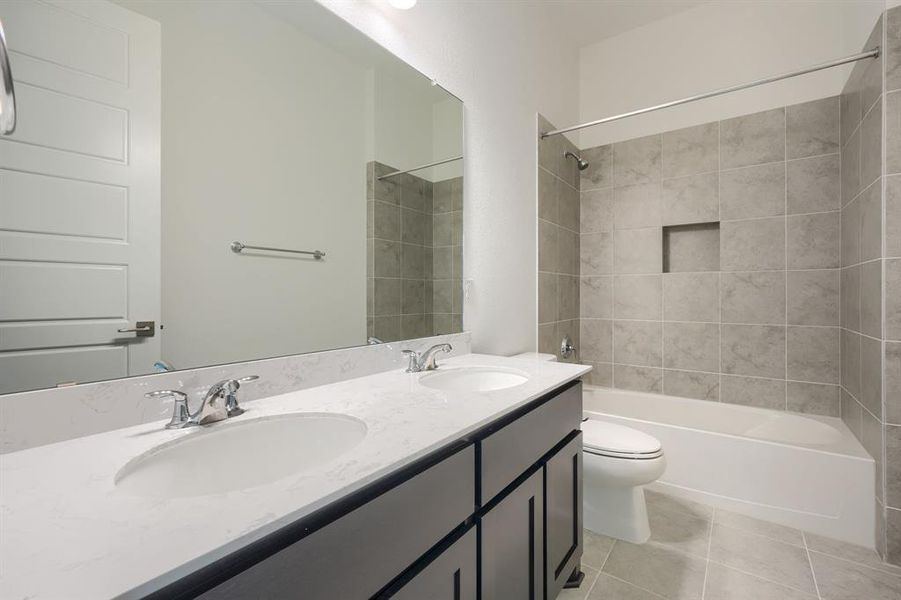 Full bathroom with tile floors, tiled shower / bath, toilet, and double sink vanity