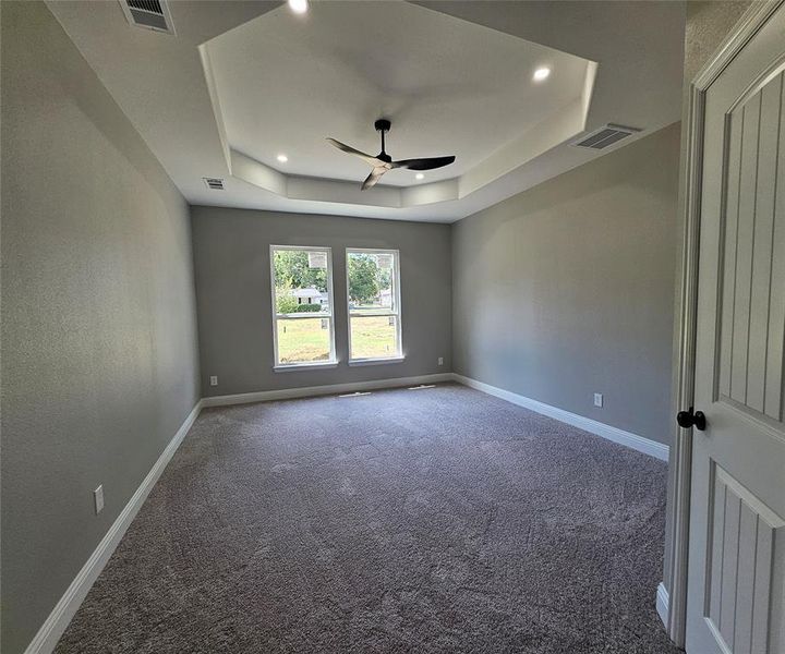 Carpeted spare room featuring a tray ceiling and ceiling fan