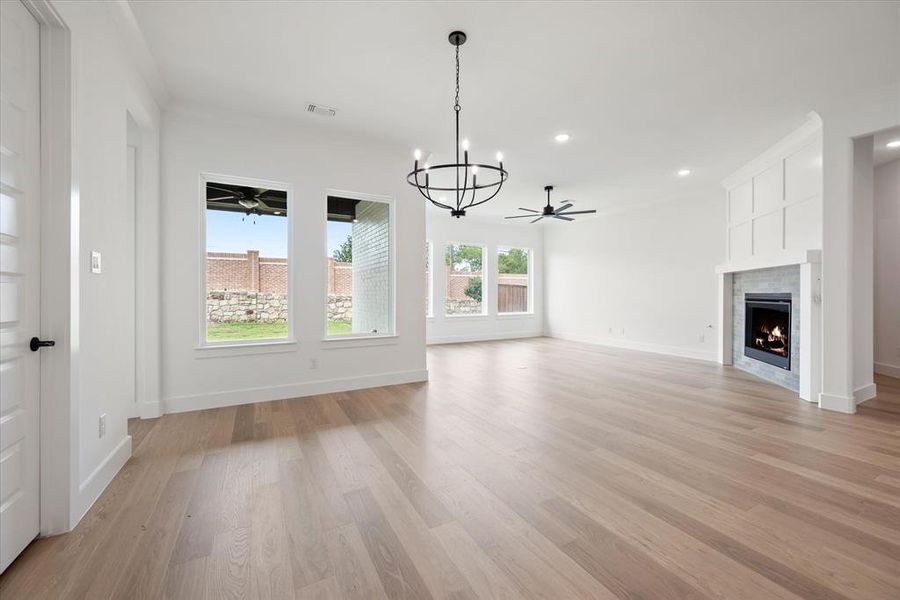 Unfurnished living room with light hardwood / wood-style flooring, a tiled fireplace, and ceiling fan with notable chandelier