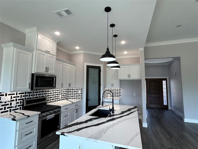 Kitchen featuring a kitchen island with sink, stainless steel appliances, sink, white cabinetry, and decorative light fixtures