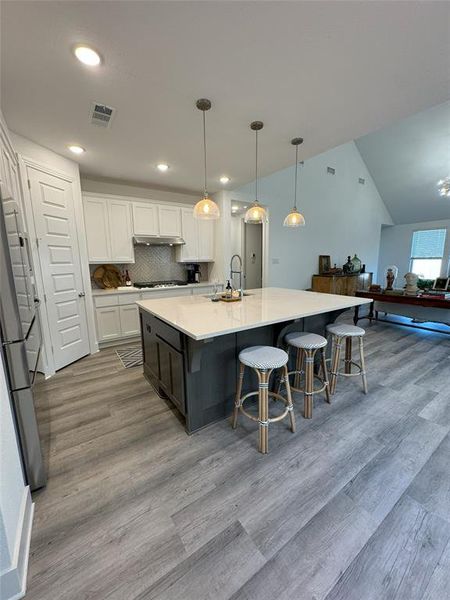 Kitchen featuring a spacious island, white cabinetry, light hardwood / wood-style floors, lofted ceiling, and decorative light fixtures