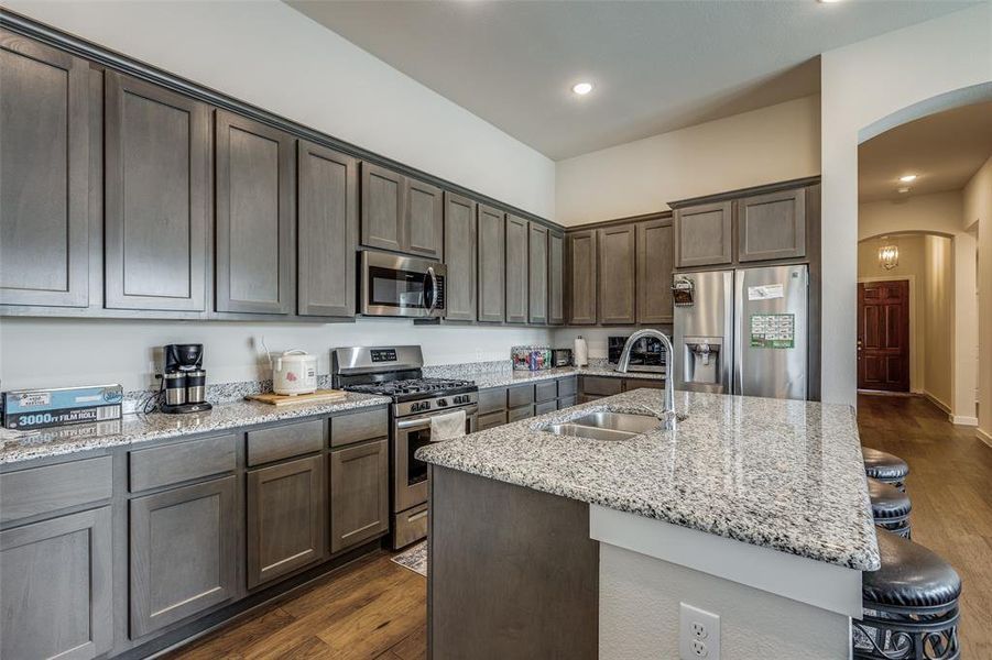 Kitchen with appliances with stainless steel finishes, sink, dark wood-type flooring, and an island with sink