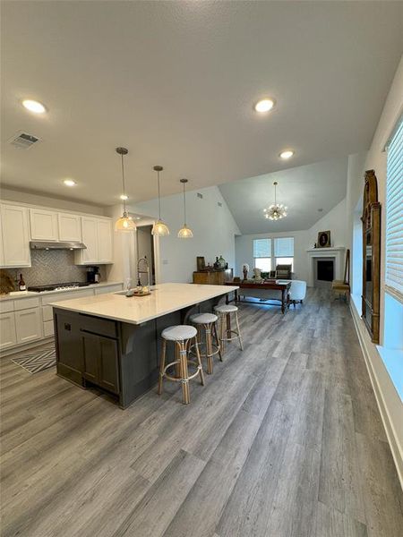 Kitchen with a large island with sink, light wood-type flooring, hanging light fixtures, lofted ceiling, and white cabinets