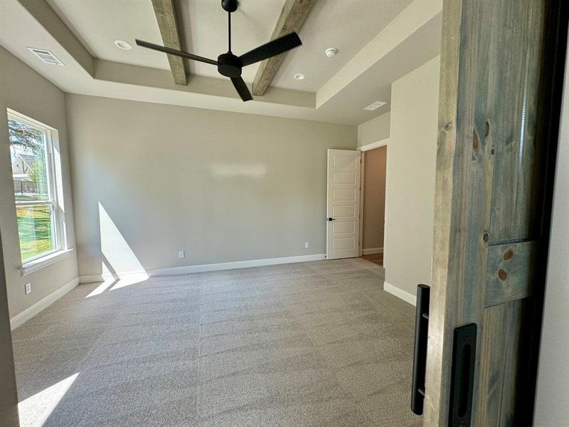 Carpeted spare room with a tray ceiling, ceiling fan, and beamed ceiling