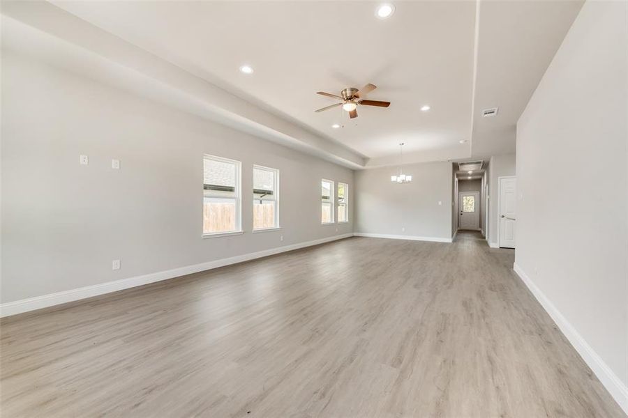 Unfurnished living room with ceiling fan with notable chandelier and light wood-type flooring