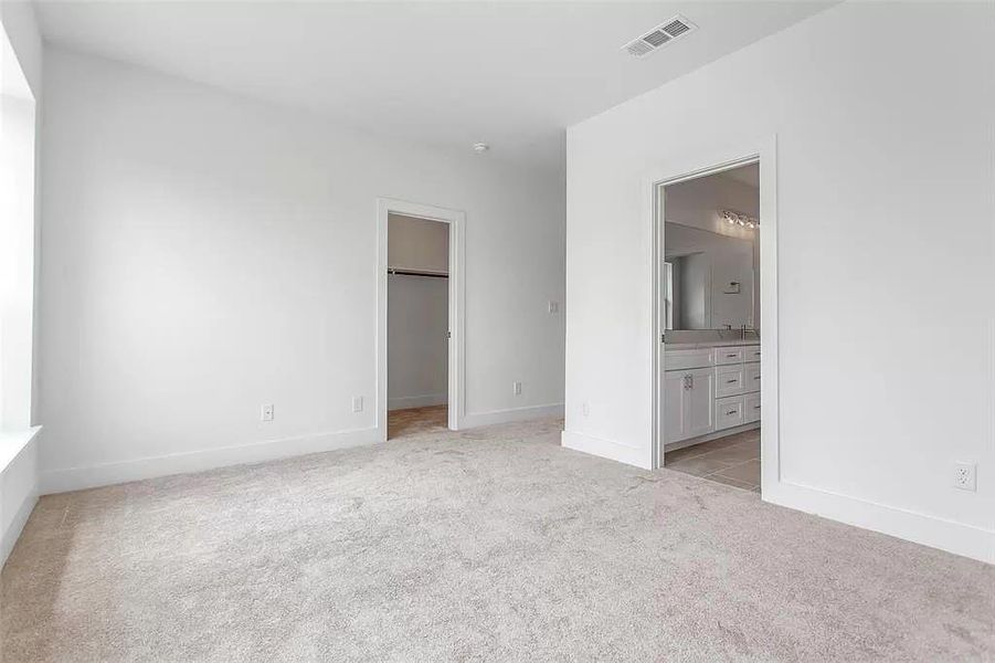 Unfurnished bedroom featuring a closet, light colored carpet, ensuite bathroom, and a spacious closet