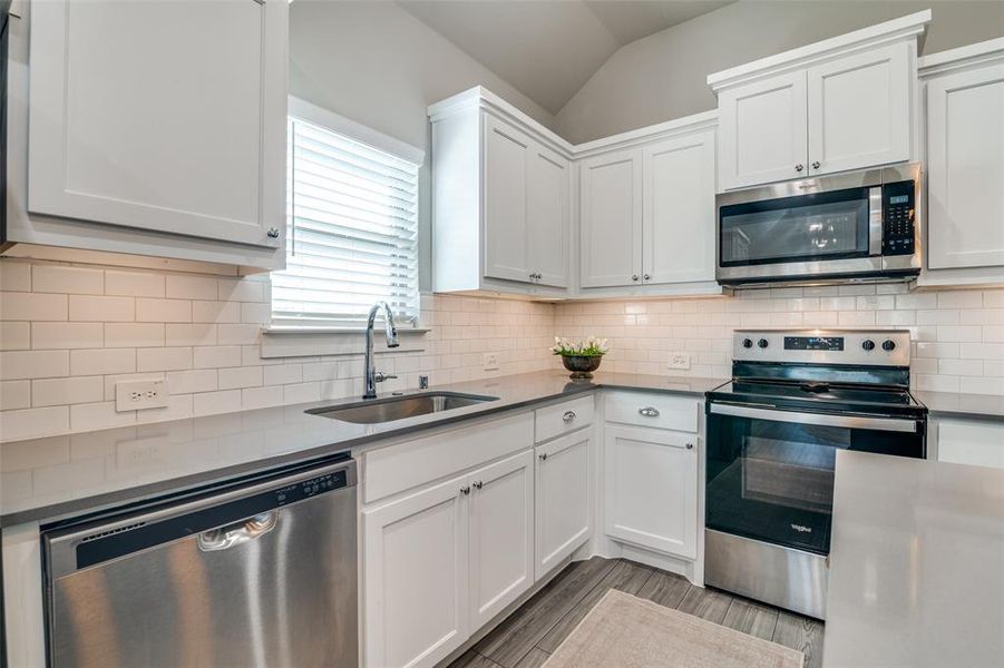 Kitchen featuring white cabinets, lofted ceiling, sink, appliances with stainless steel finishes, and decorative backsplash