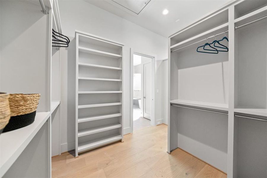 This is a spacious, modern walk-in closet featuring built-in shelves and hanging space, with a clean, minimalist design and hardwood flooring.