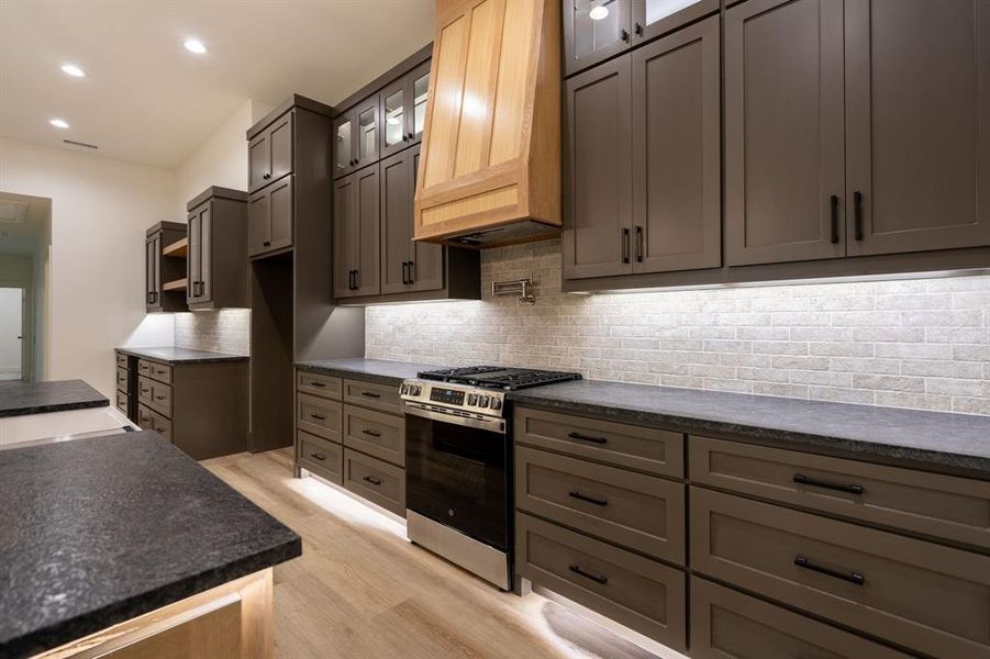 Kitchen featuring light wood-type flooring, premium range hood, backsplash, and gas range