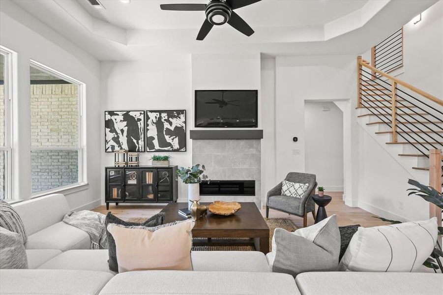 Living room featuring a tray ceiling, light hardwood / wood-style flooring, ceiling fan, and a tile fireplace