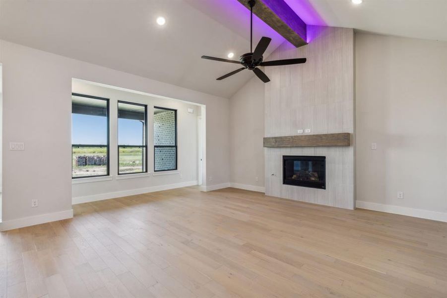 Unfurnished living room featuring ceiling fan, beamed ceiling, high vaulted ceiling, a tile fireplace, and light hardwood / wood-style floors