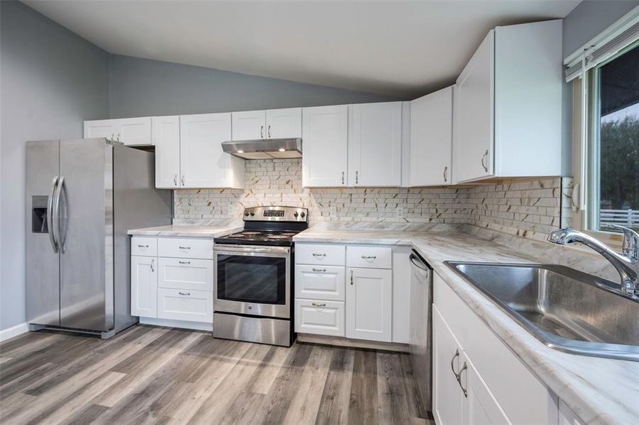 Kitchen with white cabinetry, appliances with stainless steel finishes, wood-type flooring, and lofted ceiling