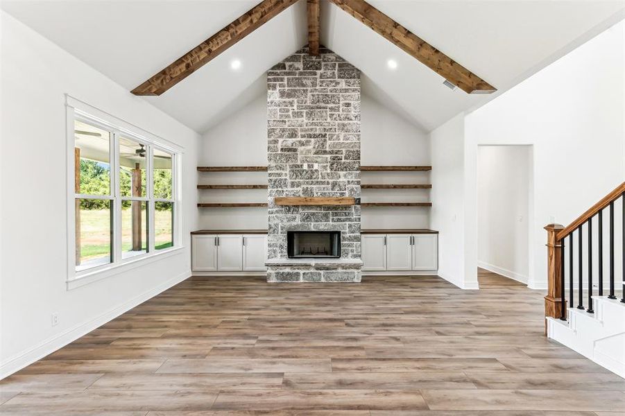 Unfurnished living room featuring light wood-type flooring, beamed ceiling, brick wall, a fireplace, and high vaulted ceiling