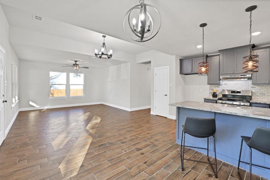 Kitchen with gray cabinets, stainless steel range with gas stovetop, light stone countertops, and dark hardwood / wood-style flooring