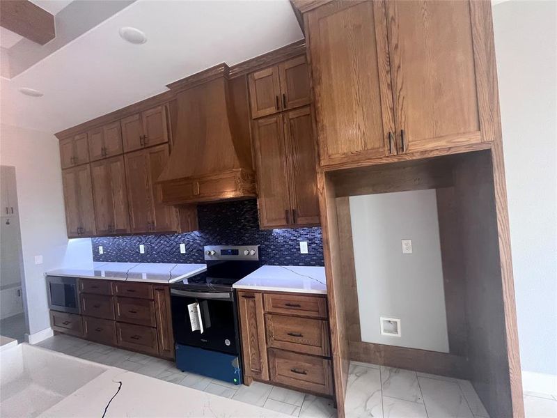 Kitchen featuring tasteful backsplash, black electric range oven, stainless steel microwave, and premium range hood