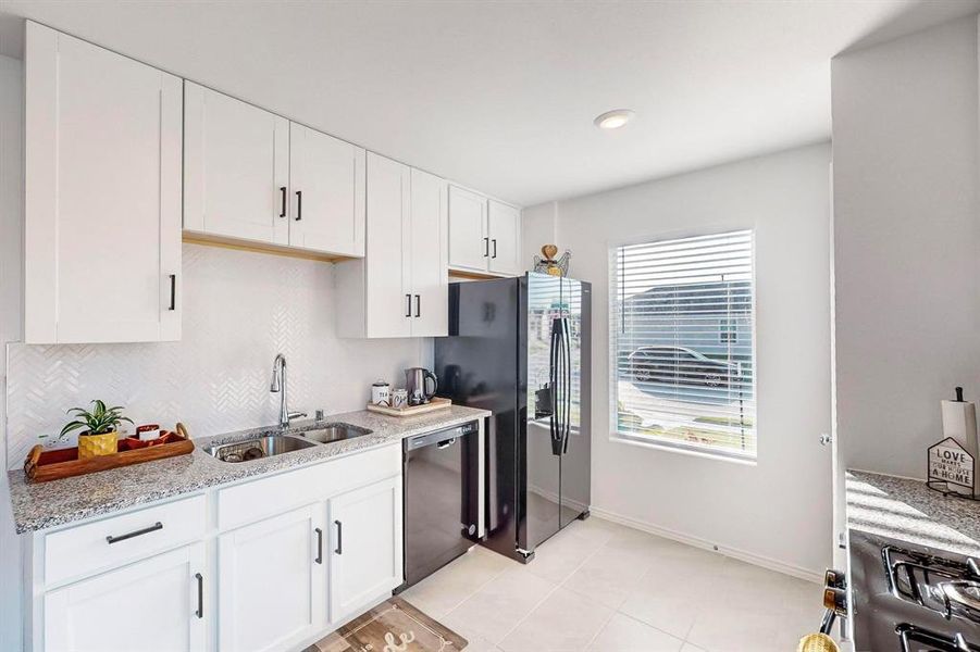 Kitchen with light stone counters, white cabinets, sink, and dishwasher