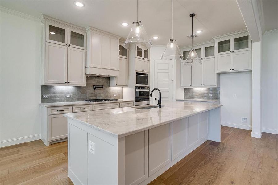 Kitchen with white cabinetry, light hardwood / wood-style floors, appliances with stainless steel finishes, backsplash, and a kitchen island with sink