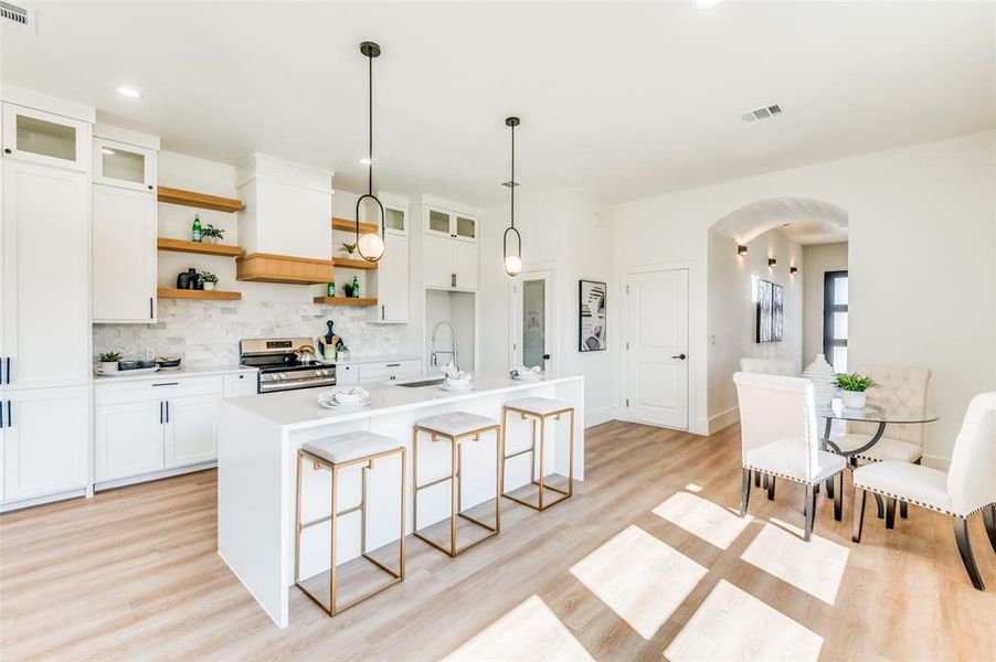 Kitchen with light hardwood / wood-style floors, stainless steel range, sink, an island with sink, and white cabinetry