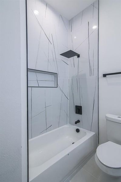 Bathroom with tiled shower / bath combo, tile patterned floors, and toilet