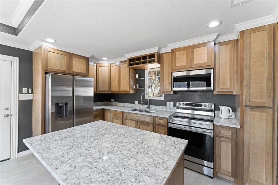 Kitchen featuring sink, a center island, stainless steel appliances, light stone counters, and ornamental molding