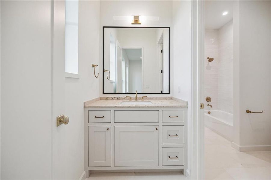 Hollywood style secondary bathroom with a clean white vanity, gold accents, and elegant wall-mounted lighting. It features a full bathtub and shower combo with simple yet sophisticated tiling.