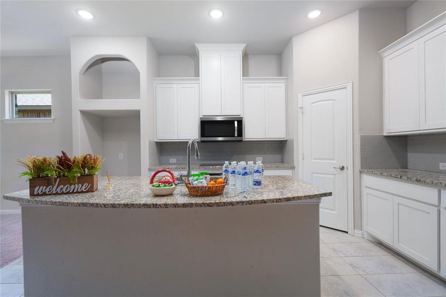 Kitchen with light tile patterned flooring, white cabinetry, tasteful backsplash, a kitchen island with sink, and light stone countertops