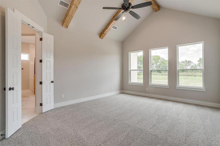 Carpeted empty room featuring beamed ceiling, ceiling fan, a healthy amount of sunlight, and high vaulted ceiling