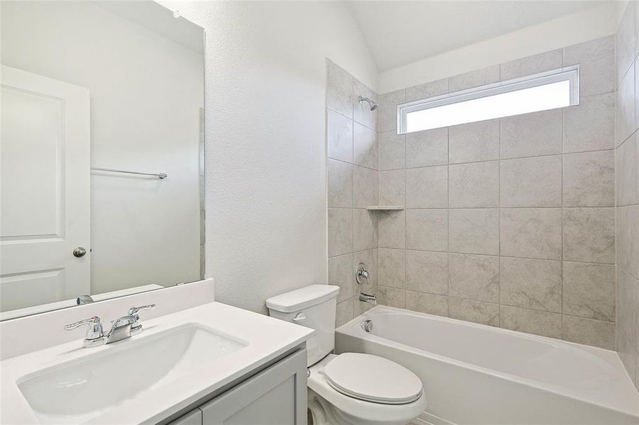 Full bathroom featuring vaulted ceiling, vanity, toilet, and tiled shower / bath combo