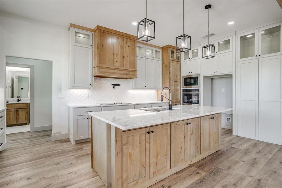 Kitchen with a kitchen island with sink, black appliances, hanging light fixtures, white cabinets, and light hardwood / wood-style floors