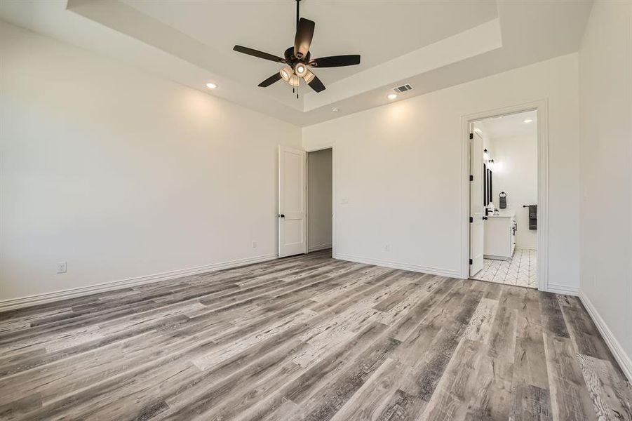 Unfurnished bedroom with a raised ceiling, light hardwood / wood-style floors, ceiling fan, and ensuite bathroom