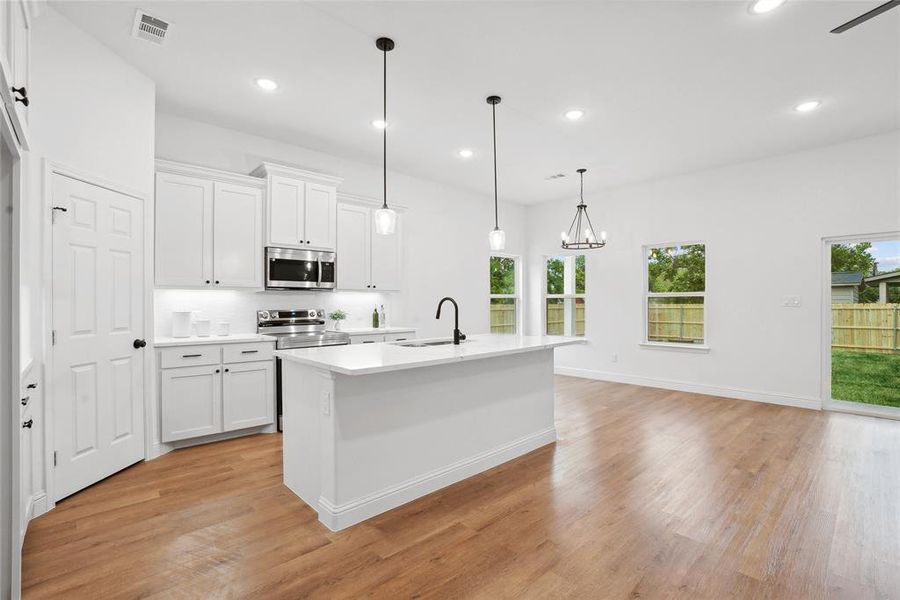 Kitchen with white cabinetry, decorative light fixtures, sink, appliances with stainless steel finishes, and a center island with sink